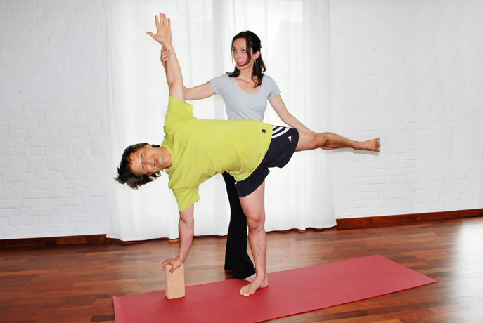 Yogalehrerin Birgit Braune assistiert Schüler bei der Yogahaltung des Halbmondes