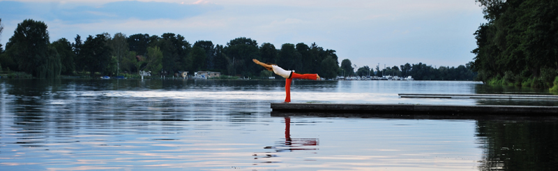 Yogalehrerin Birgit Braune in der Yogahaltung des Kriegers 3 auf einem Steg am Wasser